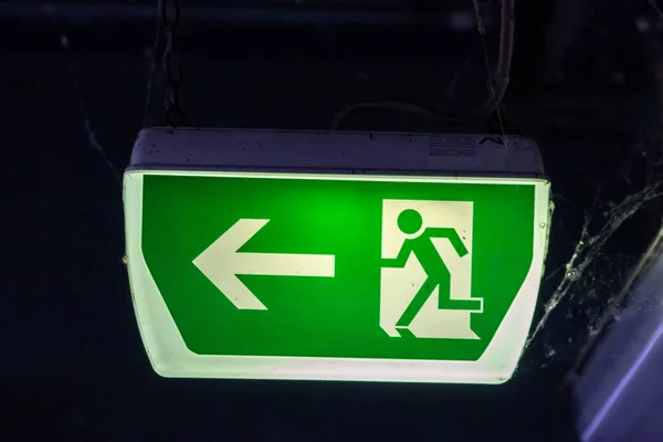 Green exit sign with running person and green arrow shows guidance system signage in a parking lot for rescue and evacuation safety in dangerous situations at ceiling rescues life in extreme danger