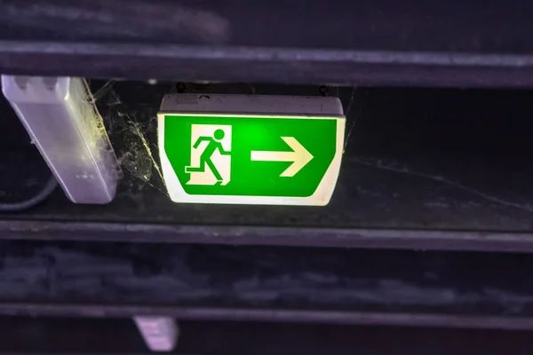 Green exit sign with running person and green arrow shows guidance system signage in a parking lot for rescue and evacuation safety in dangerous situations at ceiling rescues life in extreme danger