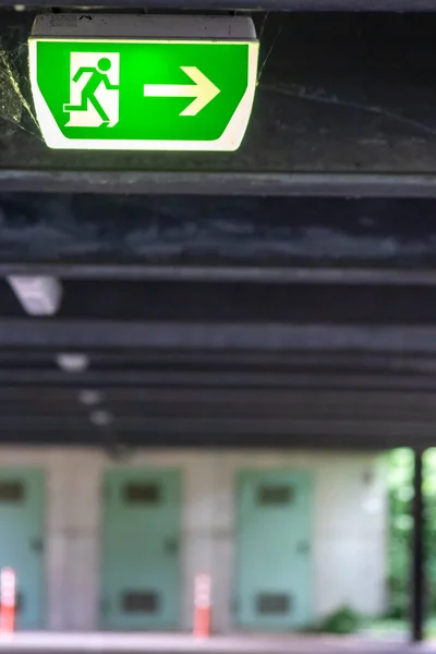 Green exit sign with running person and green arrow shows guidance system signage in a parking lot for rescue and evacuation safety in dangerous situations at ceiling rescues life in extreme danger