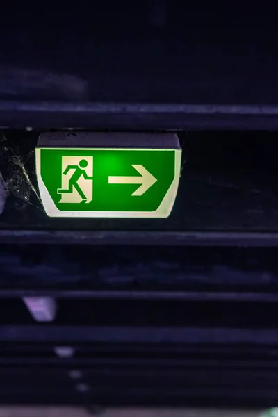 Green exit sign with running person and green arrow shows guidance system signage in a parking lot for rescue and evacuation safety in dangerous situations at ceiling rescues life in extreme danger