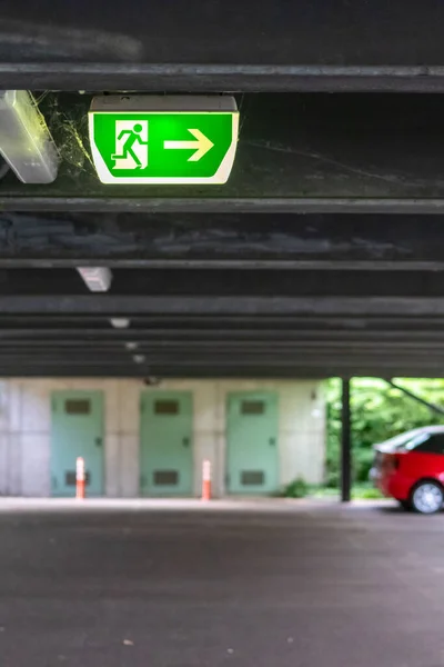 Green exit sign with running person and green arrow shows guidance system signage in a parking lot for rescue and evacuation safety in dangerous situations at ceiling rescues life in extreme danger