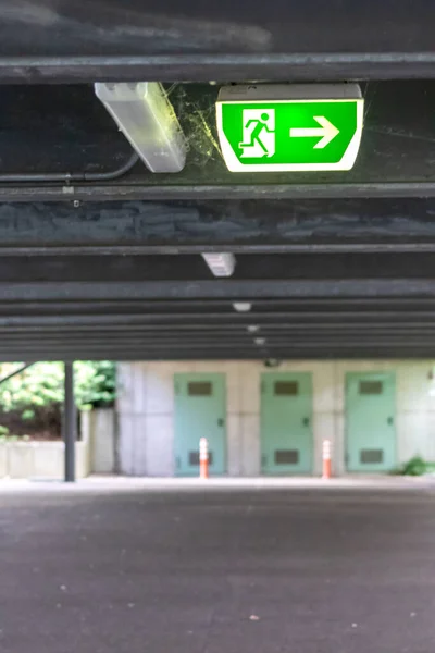 Green exit sign with running person and green arrow shows guidance system signage in a parking lot for rescue and evacuation safety in dangerous situations at ceiling rescues life in extreme danger