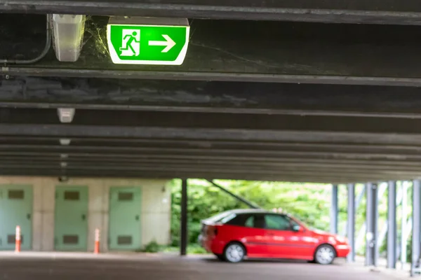 Green exit sign with running person and green arrow shows guidance system signage in a parking lot for rescue and evacuation safety in dangerous situations at ceiling rescues life in extreme danger