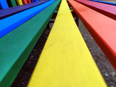 Çeşitlilik ve çeşitliliğin sembolü olarak farklı parlak renklere sahip renkli bank ve hoşgörü için gurur konsepti ve parklardaki ahşap mobilyaların mutlu yaşam tarzına sahip güzel bahçe dekorasyon koltuğu.