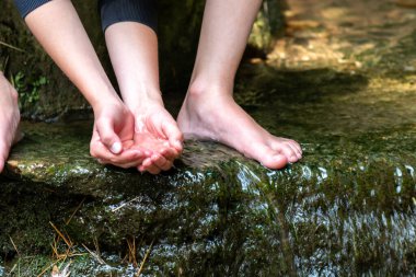 Küçük bir derede çıplak ayakla temiz suyla oynayan genç bir çocuk ayaklarını ve su kaynağını kullanarak ayak parmaklarını ve bacaklarını serinletiyor ve zen meditasyon atmosferindeki saf yaşam iksiriyle ferahlatıyor.