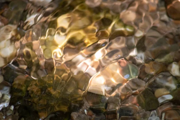 Stones in sparkling water with sunny reflections in water of a crystal clear water creek as idyllic natural background shows zen meditation, little waves and silky ripples in a healthy mountain spring