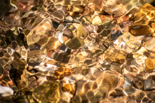 Stones in sparkling water with sunny reflections in water of a crystal clear water creek as idyllic natural background shows zen meditation, little waves and silky ripples in a healthy mountain spring