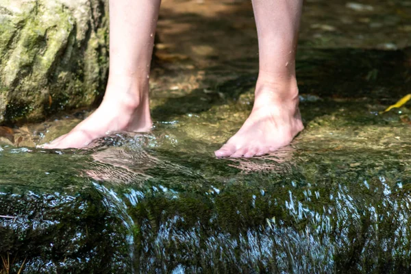 Young boy playing barefoot with clear water at a little creek using his feet and the water spring cooling his toes and legs and refreshing with the pure elixir of life in zen meditation atmosphere