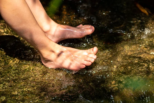 Young boy playing barefoot with clear water at a little creek using his feet and the water spring cooling his toes and legs and refreshing with the pure elixir of life in zen meditation atmosphere