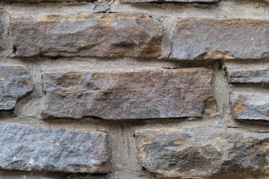 Kale duvarı gibi pürüzlü taşlarla kaplı büyük bir duvar, farklı tuğlalar, doğal arka plan ve kayalık antik zamanların duvarı, granit mineraller için eski dokular olarak taş gibi katı tuğlalar gösteriyor.