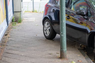 Kötü park edilmiş, kaldırımda tekerleği olan bir araba, kötü sürüş ve şehir sokaklarında park cezasıyla trafik ihlali yapan, bencil sürücüler tarafından yayalar için tehlike arz eden bir tekerlek yürüyüşü gösteriyor.