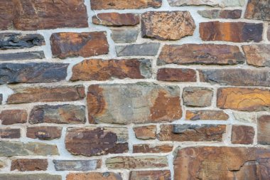 Kale duvarı gibi pürüzlü taşlarla kaplı büyük bir duvar, farklı tuğlalar, doğal arka plan ve kayalık antik zamanların duvarı, granit mineraller için eski dokular olarak taş gibi katı tuğlalar gösteriyor.
