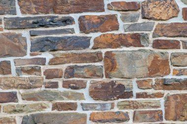 Kale duvarı gibi pürüzlü taşlarla kaplı büyük bir duvar, farklı tuğlalar, doğal arka plan ve kayalık antik zamanların duvarı, granit mineraller için eski dokular olarak taş gibi katı tuğlalar gösteriyor.