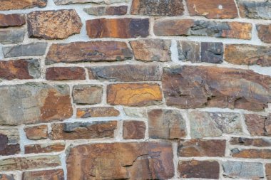Kale duvarı gibi pürüzlü taşlarla kaplı büyük bir duvar, farklı tuğlalar, doğal arka plan ve kayalık antik zamanların duvarı, granit mineraller için eski dokular olarak taş gibi katı tuğlalar gösteriyor.