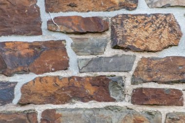 Kale duvarı gibi pürüzlü taşlarla kaplı büyük bir duvar, farklı tuğlalar, doğal arka plan ve kayalık antik zamanların duvarı, granit mineraller için eski dokular olarak taş gibi katı tuğlalar gösteriyor.