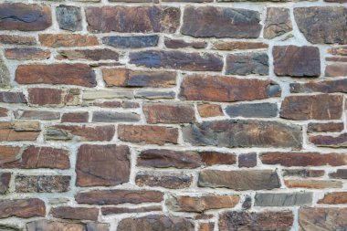 Kale duvarı gibi pürüzlü taşlarla kaplı büyük bir duvar, farklı tuğlalar, doğal arka plan ve kayalık antik zamanların duvarı, granit mineraller için eski dokular olarak taş gibi katı tuğlalar gösteriyor.