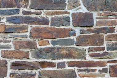 Kale duvarı gibi pürüzlü taşlarla kaplı büyük bir duvar, farklı tuğlalar, doğal arka plan ve kayalık antik zamanların duvarı, granit mineraller için eski dokular olarak taş gibi katı tuğlalar gösteriyor.