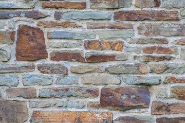 Kale duvarı gibi pürüzlü taşlarla kaplı büyük bir duvar, farklı tuğlalar, doğal arka plan ve kayalık antik zamanların duvarı, granit mineraller için eski dokular olarak taş gibi katı tuğlalar gösteriyor.