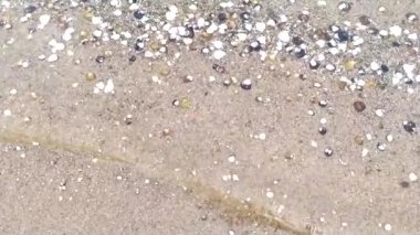 Deniz kıyısındaki küçük dalgalar ve deniz kabukları ile nehir kıyısındaki sakin manzara okyanus veya nehir manzaralı gevşeme tatilini ve plaj arka planlarında dikişsiz döngü ve çakıl taşlarıyla yavaş çekim göstermektedir.