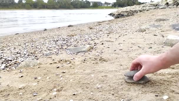 Evropští muži ručně stavění kámen stack na břehu řeky v klidné atmosféře s klidným pohybem prstů a oblázků ukazuje zen jako harmonie a relaxace v přírodě a pobřeží kamenné pyramidy