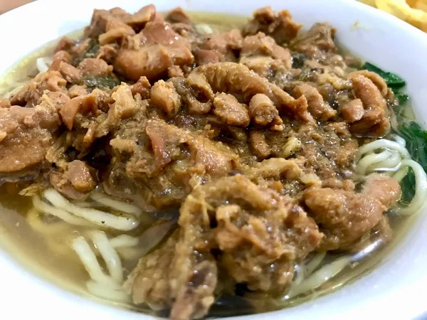 Taze et ve taze kahverengi et suyuyla kaplanmış sıcak erişte kasesi, taze sebzelerle servis edilmiş, sıcak ve lezzetli bir sokak yemeği gösteriyor..