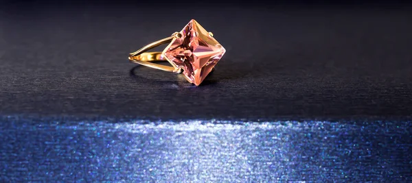 Gold ring with a pink gem on a blue background.