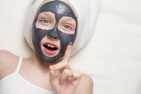 Girl with a clay mask on her face with a towel on her head.