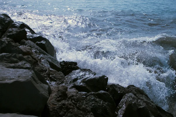 Ocean surf on the black stones — стоковое фото