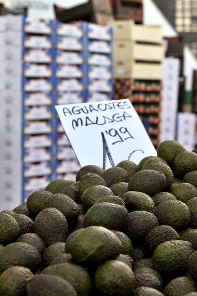 Bir market tezgahında karton üzerine fiyat yazan bir avuç avokado yakın plan..