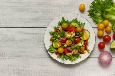 Taze sebzeler: kırmızı ve sarı domates, mor soğan, yeşil marul ve salatalık, tabakta kırmızı biber. Yukarıdan görüntüle.