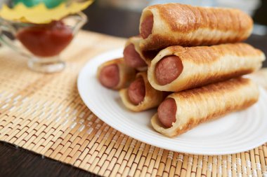 Kızarmış hamurda sosis. Sosisli kızarmış turta. Tereyağlı hamurun ince şeritlerine sarılmış..