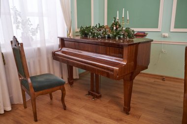 Yeni yıl ladin dallarıyla süslenmiş bir kuyruklu piyano ve yanında da bir şamdan, yeşil bir sandalye.