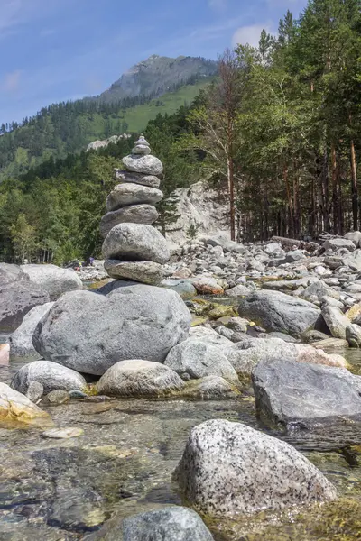 Piramide van stenen aan de rivieroever tegen een berglandschap. — Stockfoto