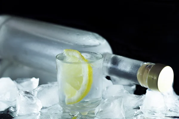 Vista de close-up de garrafa de vodka com óculos em pé no gelo em preto — Fotografia de Stock