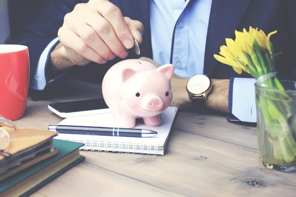 Man en piggy bank op houten tafel — Stockfoto