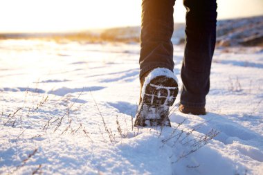 Adam gün batımında karda yürüyor.