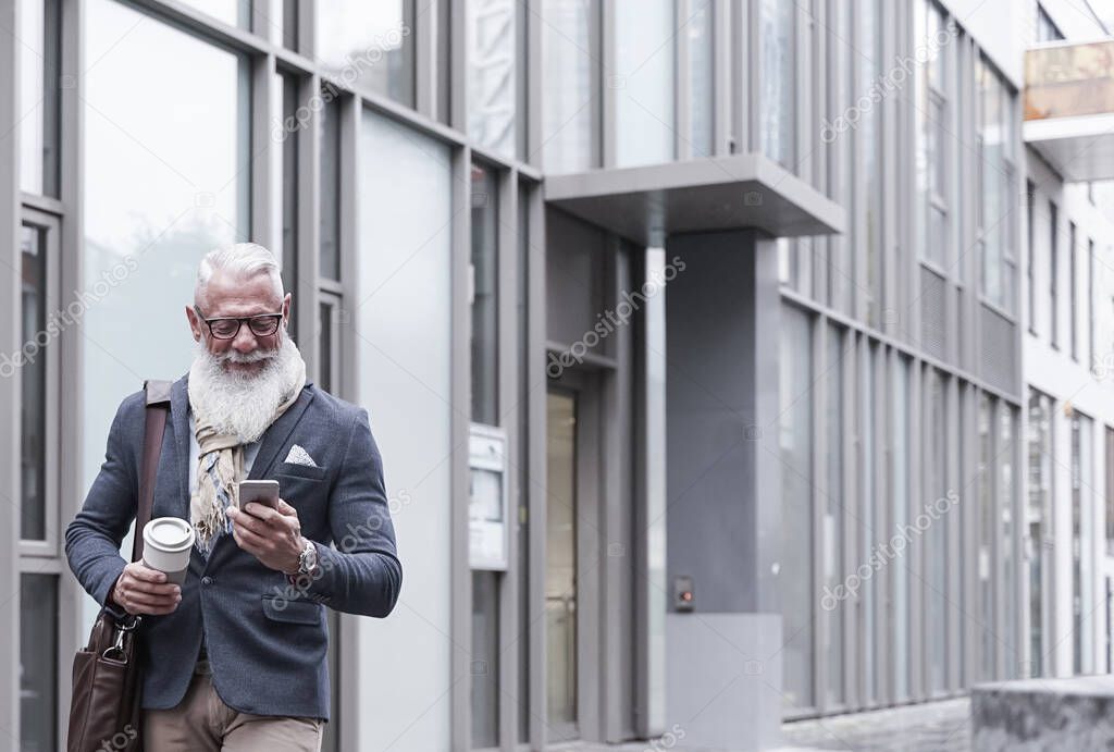 Happy senior businessman looking cellular phone and drinking a hot coffee after of the work. Job and fashion lifestyle concept.