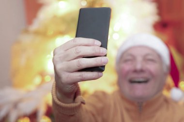 Noel Baba şapkalı yaşlı adam çok renkli arka planda bir Noel videosu arıyor. Teknoloji ve Noel konsepti.