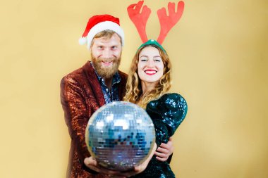 Kırmızı şapkalı neşeli genç çift sarı arka planda izole edilmiş yeni yıl partisini kutluyor. Noel, yeni yıl ve parti konsepti.