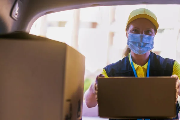 Coronavirus (COVID-19) salgını sırasında kadın servis kuryesi, karton kutularla çalışan virüs enfeksiyonundan korunmak için sağlık maskesi takan kurye.
