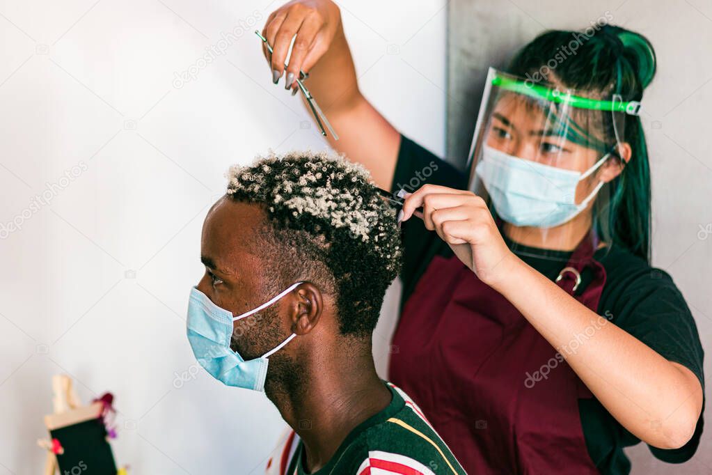 Professional hairstylists with masks on their faces, doing a hair job on a man in a beauty salon during COVID-19 pandemic.