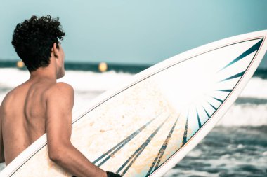 Sahilde sörf tahtası tutan bir sörfçüyü yakından çek. Sörf tahtasıyla dalgalara bakan bir sörfçü. Spor ve tatil konsepti.