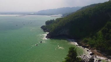 Karang Agung Sahili, Kebumen, Central Java, Endonezya 'nın insansız hava aracı görüntüsü. Kıyı şeridi yoğun ağaçlarla ve okyanustan gelen dalgalarla çevrili mercan kayalarıyla çevrilidir..