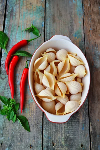 Pasta snäckor i keramisk form, chili peppar och basilika på ett trä — Stockfoto