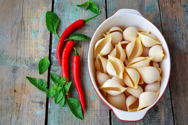 Makaron muszle w ceramicznej formie, papryka chili i bazylia na drewnianym — Zdjęcie stockowe