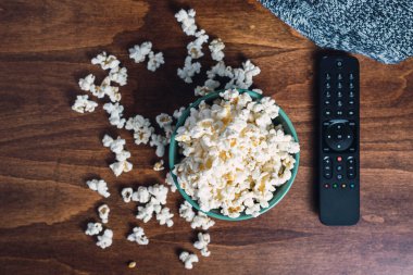 Patlamış mısır, uzaktan kumanda ve battaniye ahşap masa üzerinde kanepe, battaniye ve film, evde dinlenme ve rahatlama kavramı