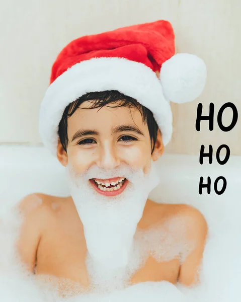 Uśmiechnięty Chłopiec Wannie Kapeluszem Mikołaja Piankową Brodą Koncepcyjne Boże Narodzenie — Zdjęcie stockowe
