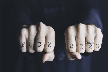 Male hands with the expression fuck 2020 on their knuckles. Conceptual of new year, christmas and end of year