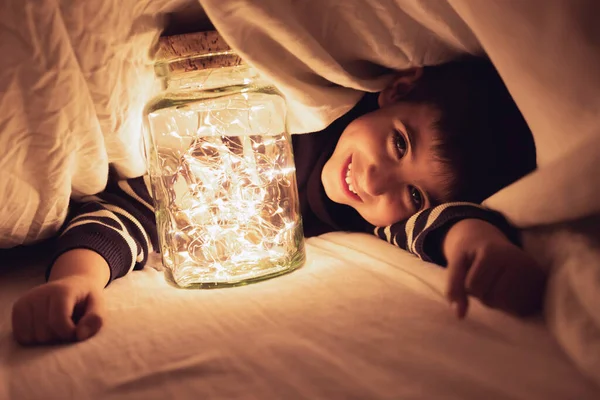 Niño Juega Bajo Sábana Con Una Olla Luces Cálidas Conceptual Imagen De Stock