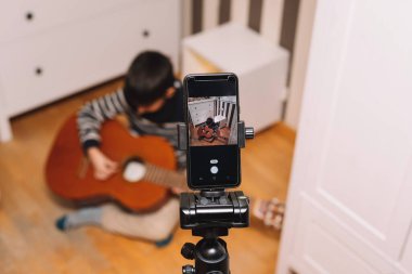 Çocuk klasik gitar çalmayı uzaktan öğreniyor ve uygulamalarını mobil yaşam tarzı ve çevrimiçi öğrenme kavramlarıyla kaydediyor.